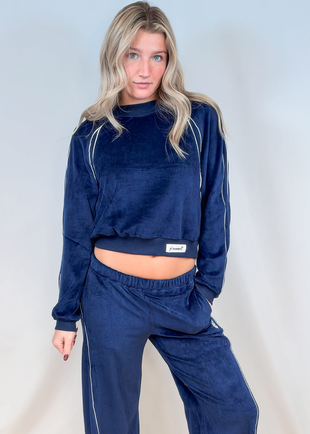 Woman wearing matching blue velour set with white piping on plain background