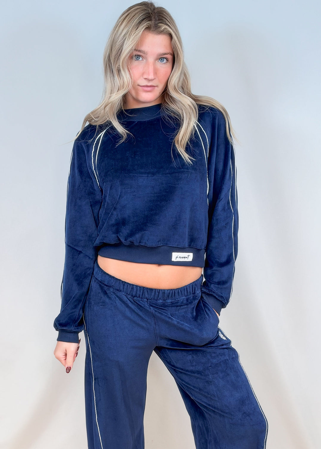 Woman wearing matching blue velour set with white piping on plain background