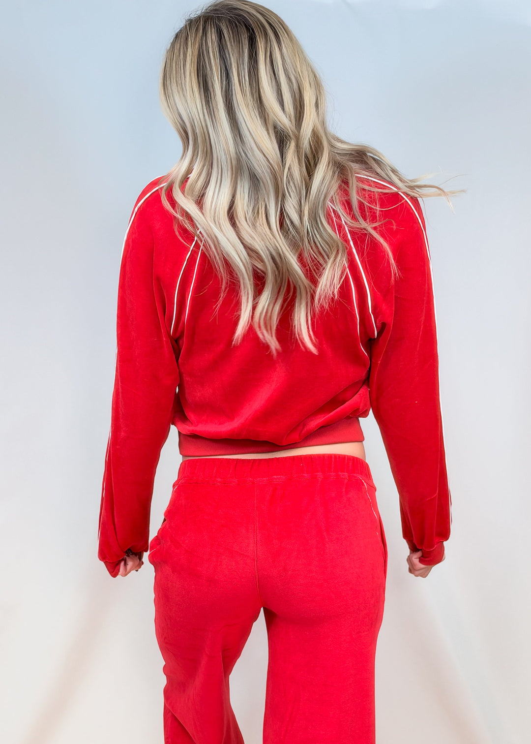 Woman shown from back view wearing red matching velour set with white piping on plain background