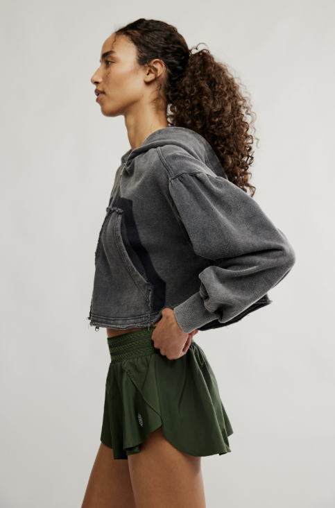 Woman wearing green shorts and grey hoodie on white background