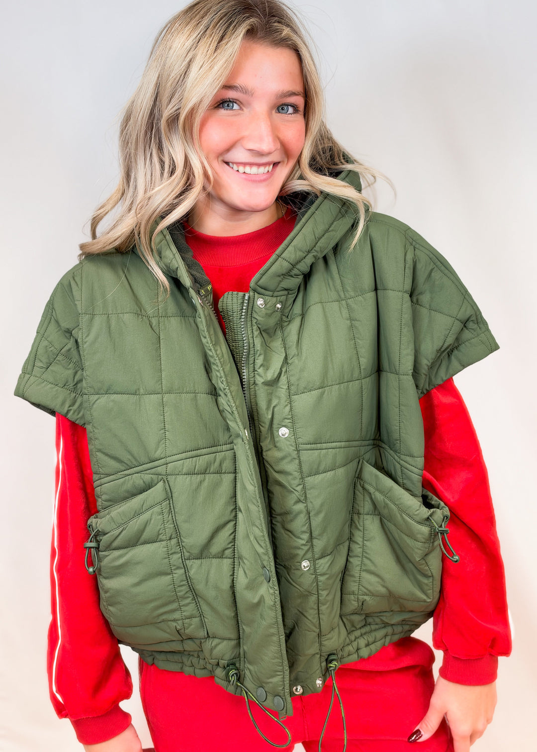 Woman wearing matching red velour set with olive green quilted puffy vest on plain background
