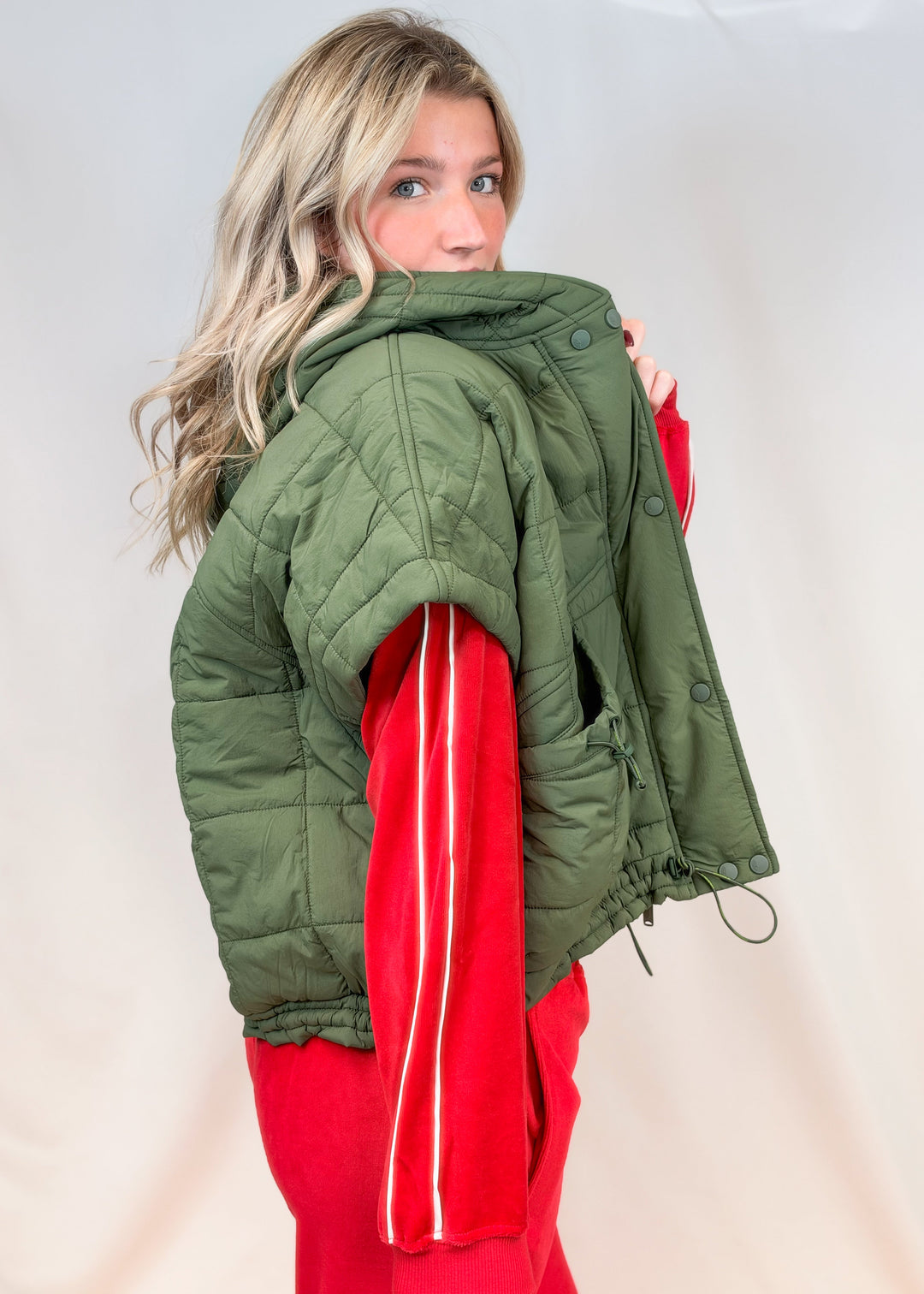 Woman shown from side view wearing matching red velour set with olive green puffy quilted vest on plain background