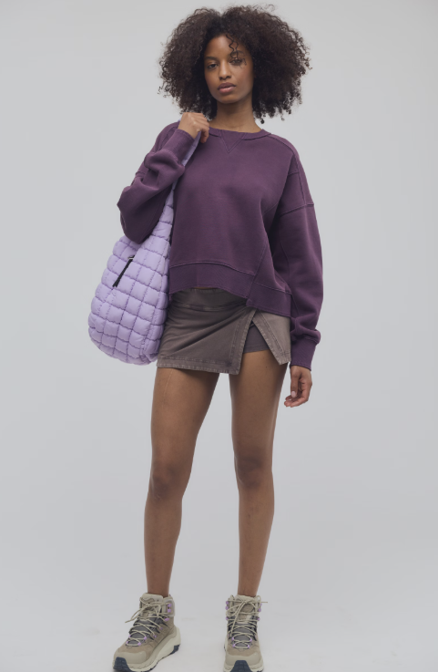 Woman wearing purple sweatshirt with brown skirt on plain background
