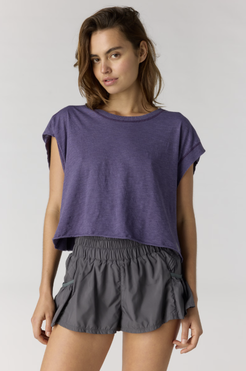 Woman wearing purple short sleeve shirt with black shorts on plain background
