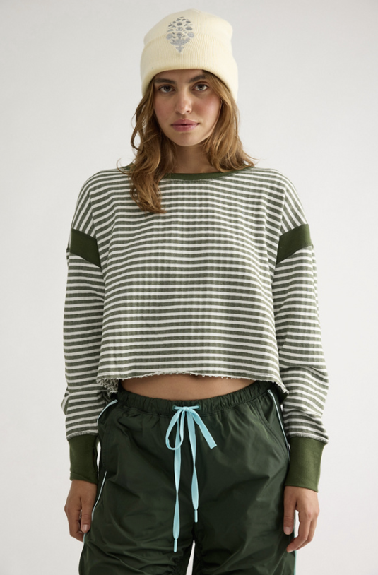 Woman wearing green and white stripe top with green pants and ivory beanie on plain background