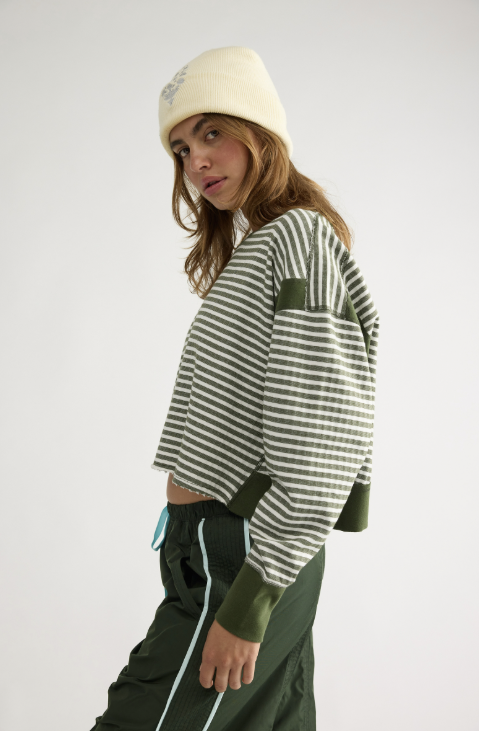 Woman shown from side view wearing green and white stripe shirt, green pants and ivory beanie on plain background