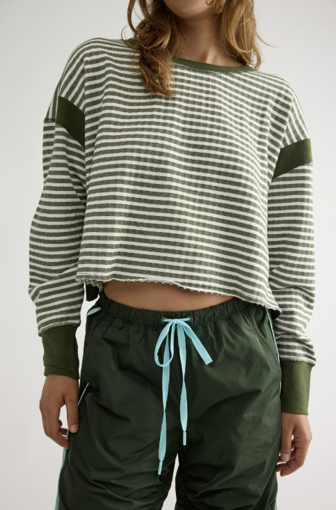 A cropped long-sleeve knit top with horizontal olive green and white stripes, featuring solid olive green sleeve patches and cuffs, worn by a model with dark green drawstring pants.