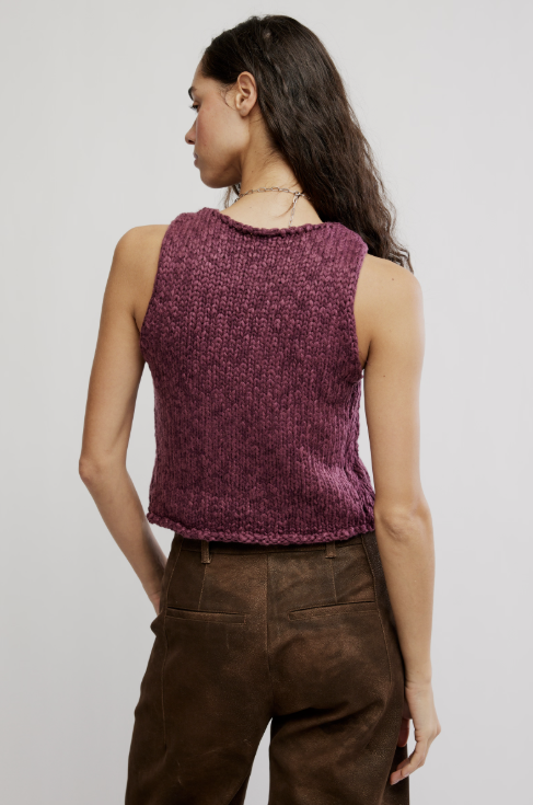 A woman shown from the back wearing a sleeveless, textured knit top in a heathered plum-purple color, paired with brown pants, against a plain light gray studio background.