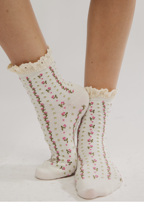 Person wearing pink floral ankle length ruffle socks on plain background