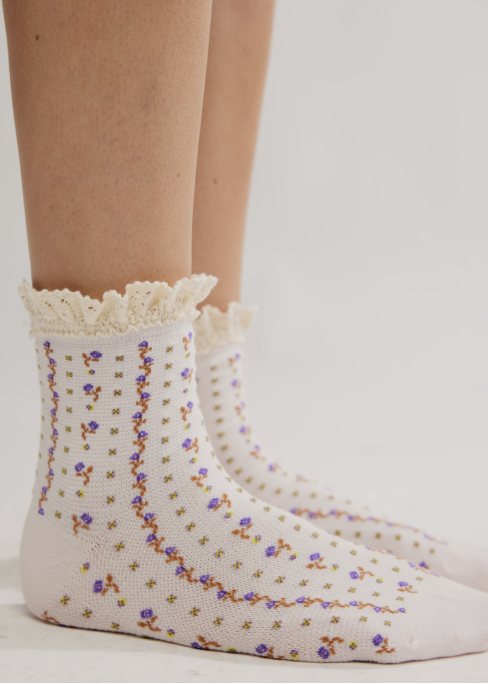 Person wearing pair of purple floral ankle length ruffle socks on plain background