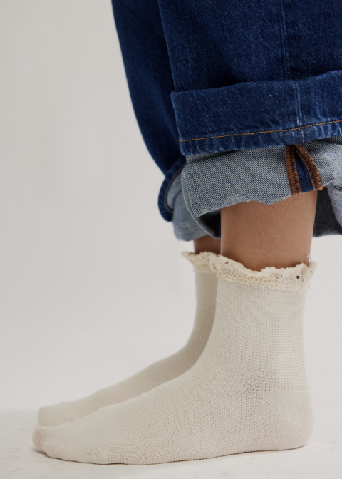 Person wearing jeans and ankle length ruffle socks on plain background