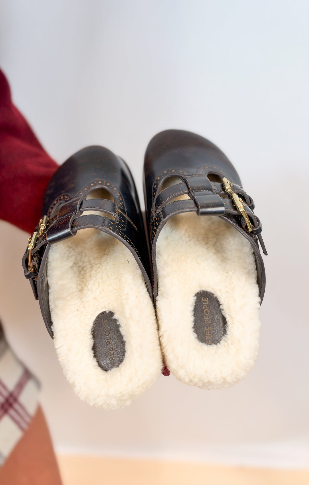 Person holding brown leather mules with shearling inners on plain background