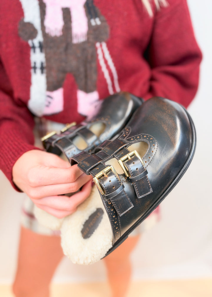 Person holding brown leather mule shoes with shearling inner on plain background