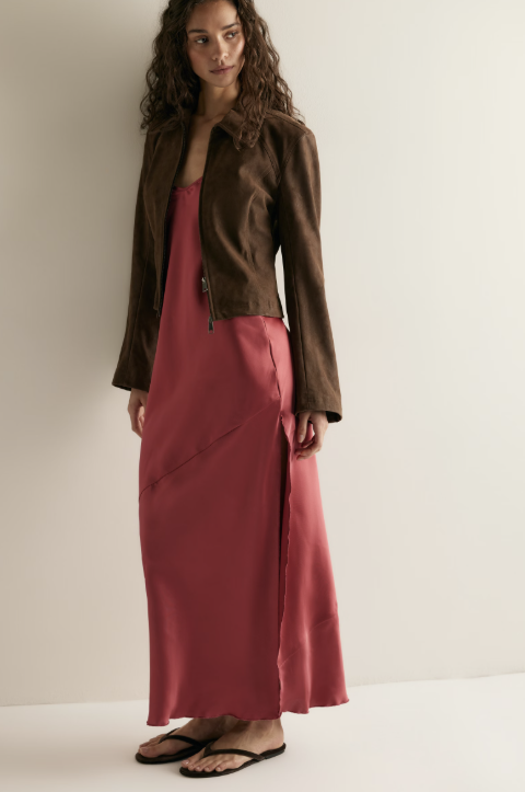 Woman wearing red satin dress with brown jacket on plain background