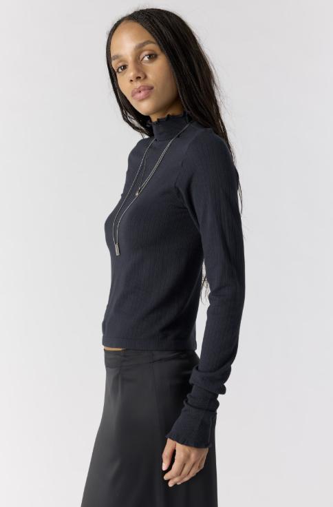Woman shown from side view wearing black body fitting mock neck top with black skirt on plain background