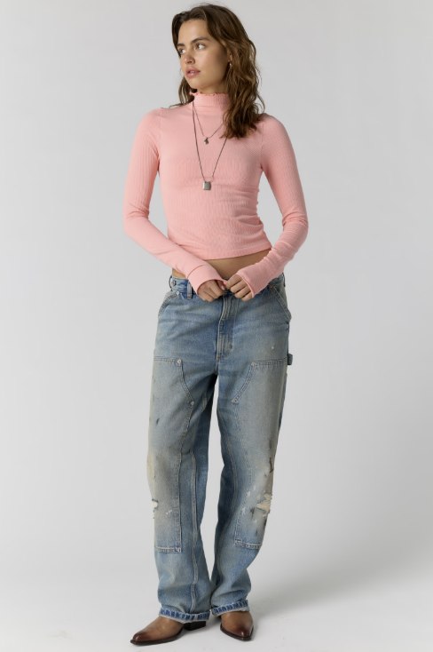 Woman wearing pink body fitting mock neck with jeans on plain background