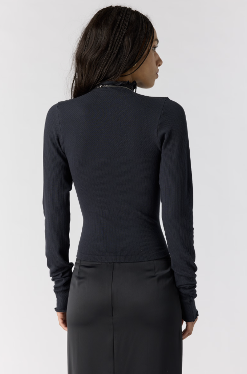 Woman shown from back view wearing black body fitting mock neck top with black skirt on plain background