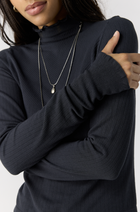 Close up of woman wearing black body fitting mock neck top on plain background