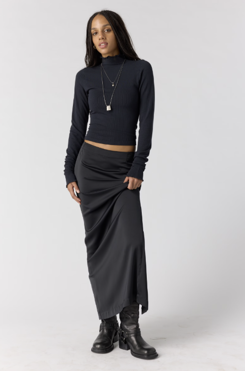 Woman wearing black body fitting mock neck top with black skirt on plain background
