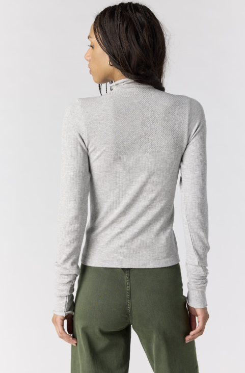 Woman shown from back view wearing grey body fitting mock neck top with green pants on plain background