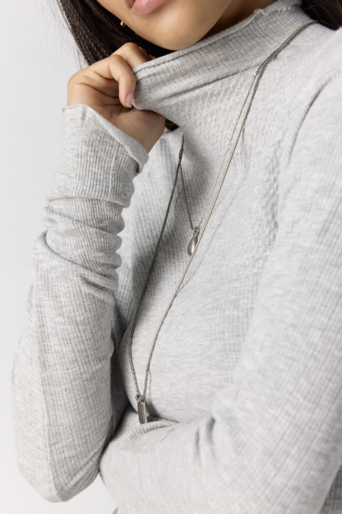 Close up of woman wearing grey body fitting mock neck top on plain background