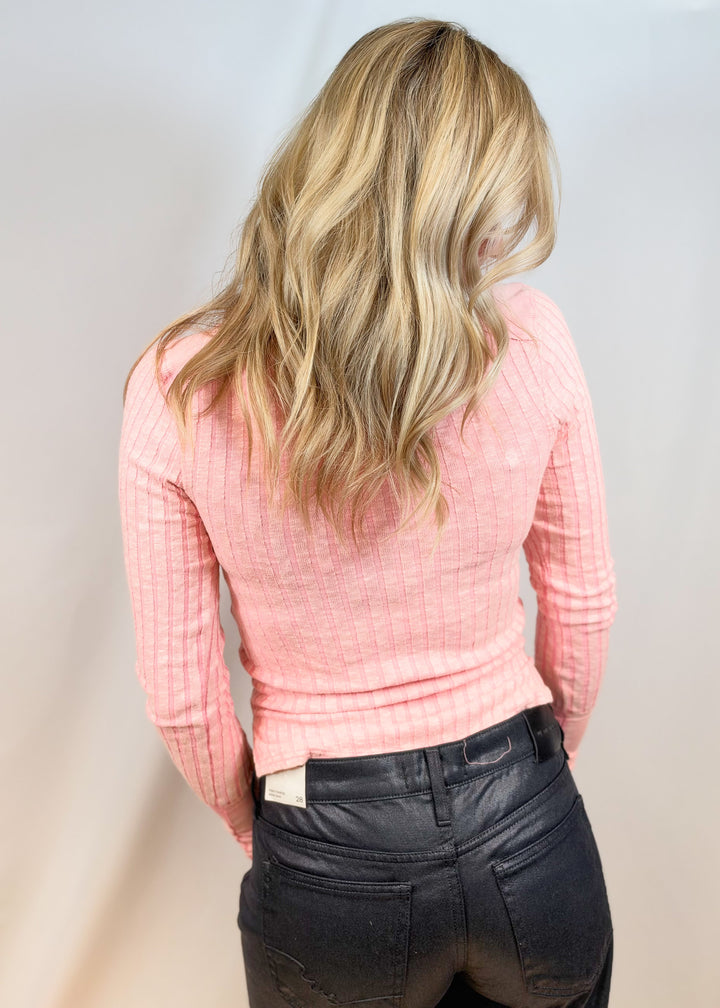 Woman shown from back view wearing pink top and black pants on plain background