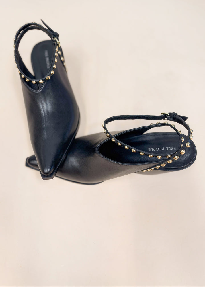 Pair of black leather pointed toe heels with gold studded wraps on plain background