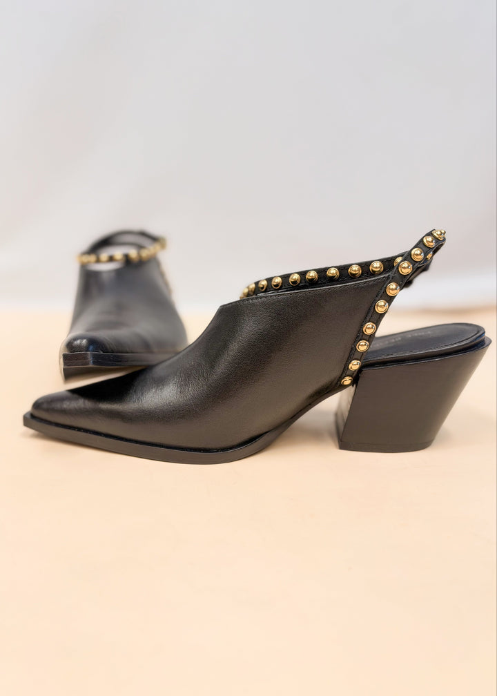 Pair of black leather pointed toe heels with gold studded wraps on plain background