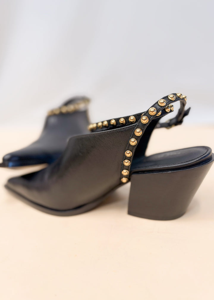 Pair of black leather pointed toe heels with gold studded leather wraps on plain background