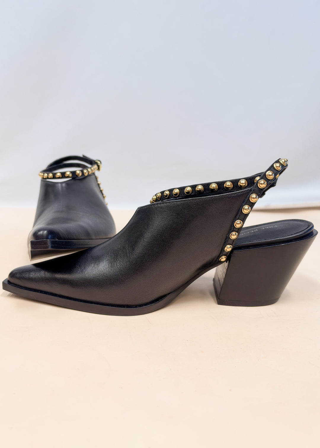 Pair of black leather pointed toe heels with gold studded wraps on plain background