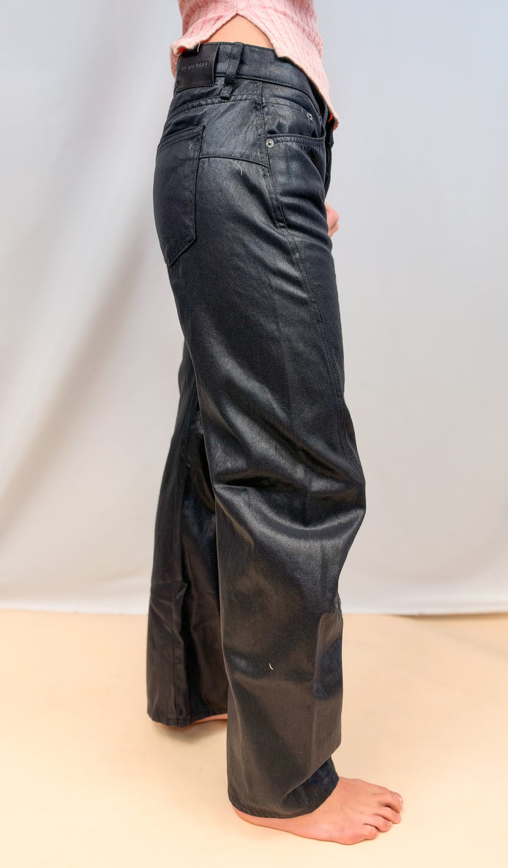 Woman shown from side view wearing black coated jeans on plain background