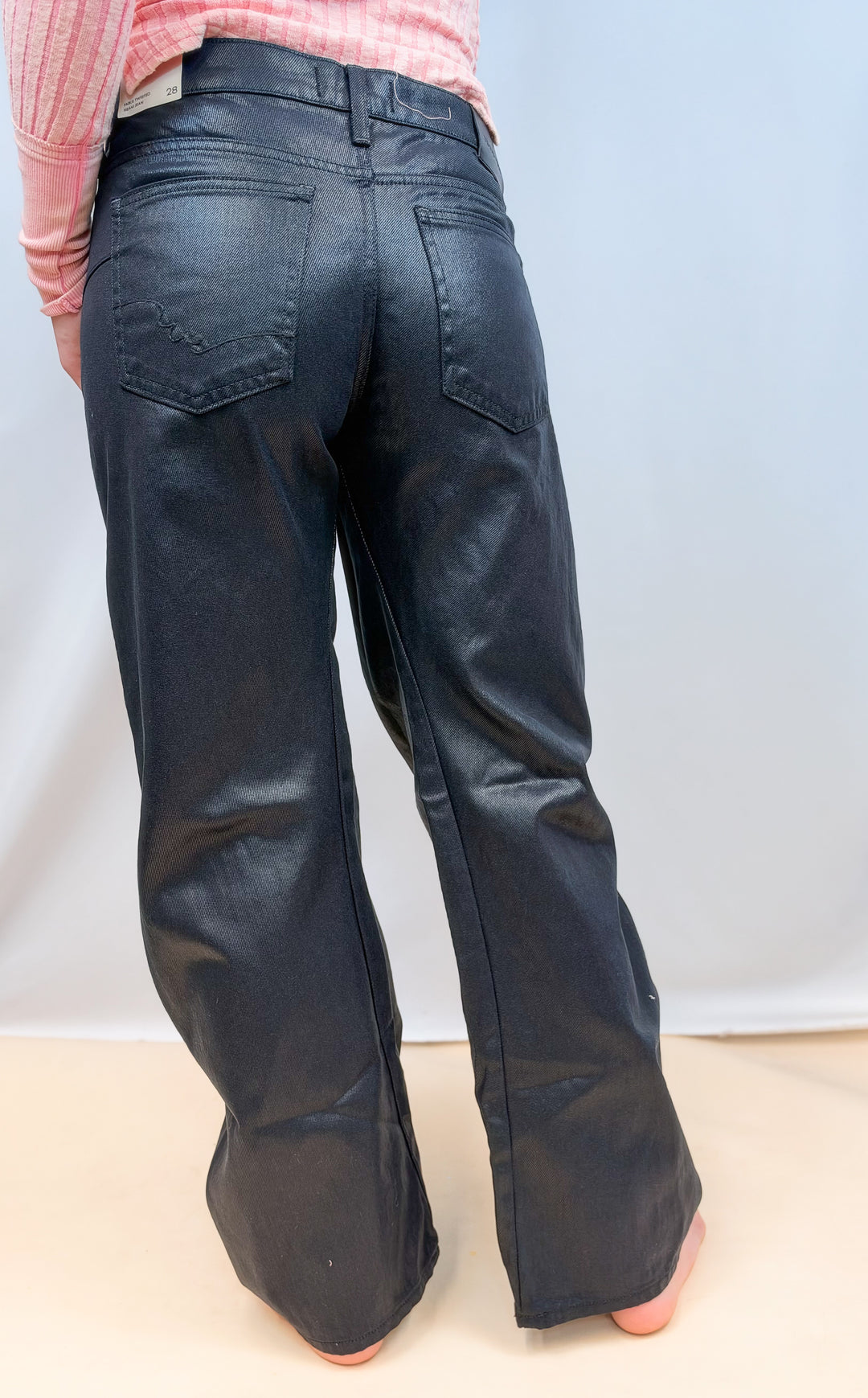 Woman shown from back view wearing black coated jeans on plain background