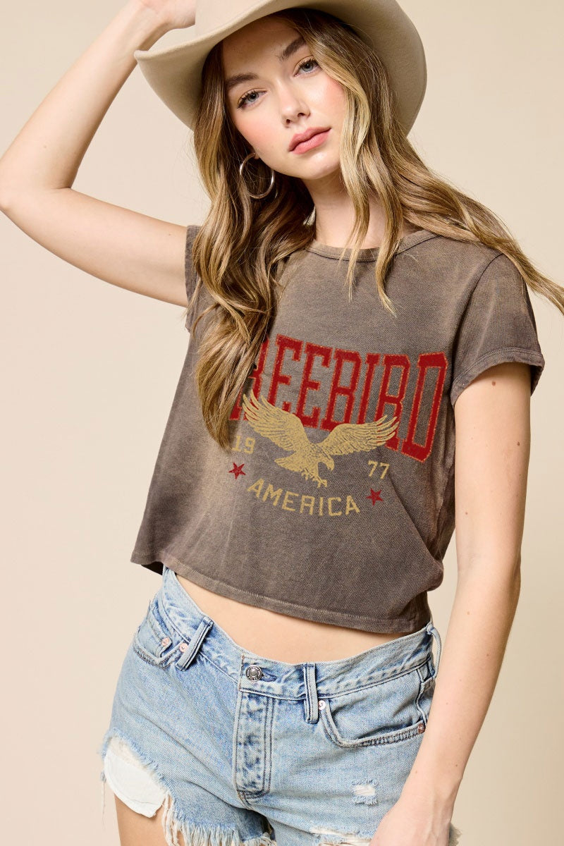 Woman wearing brown tshirt with freebird detail on plain background
