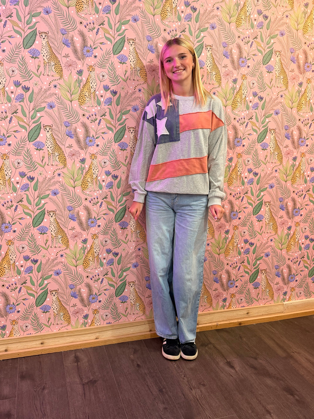Person wearing a colorful sweater and jeans standing against a patterned wall.