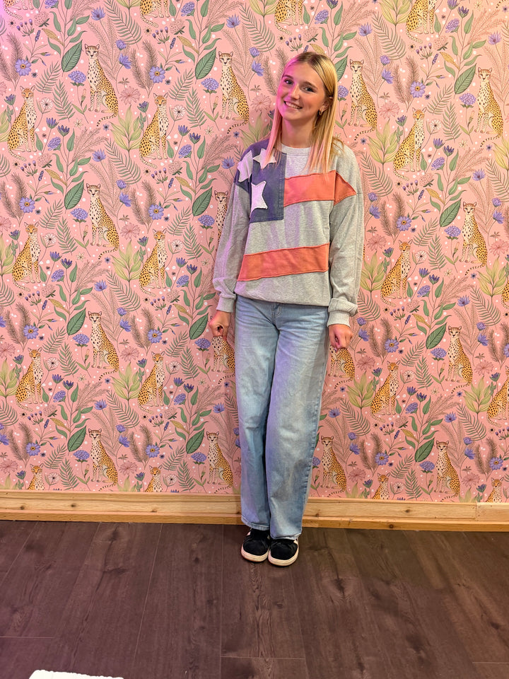 Person wearing a colorful sweater and jeans standing against a pink wall with animal and floral pattern.