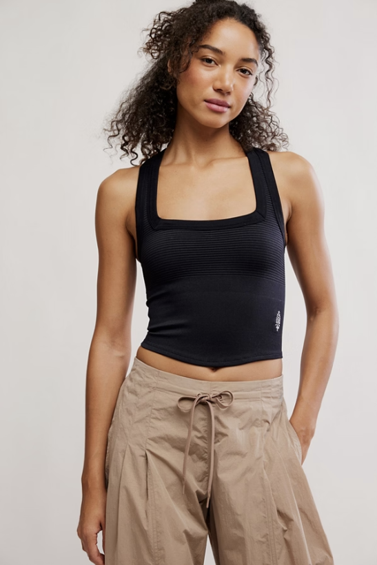 Woman wearing a black tank top and beige pants against a plain background