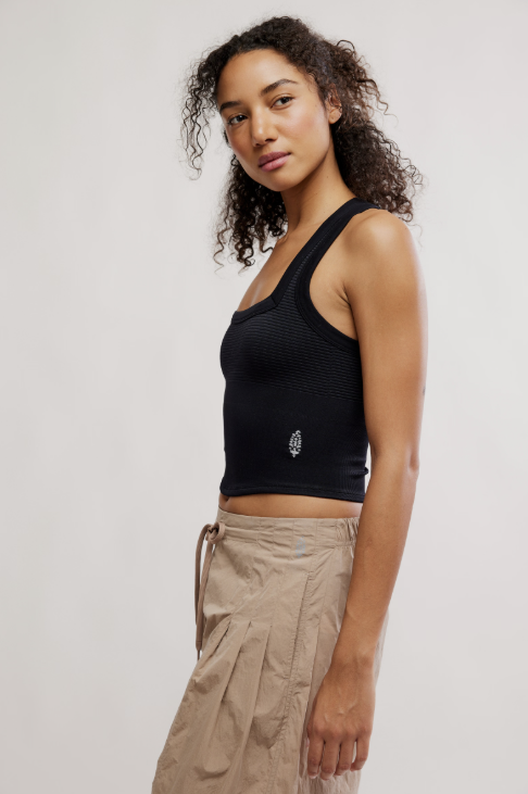 Woman wearing a black tank top and beige pants against a white background