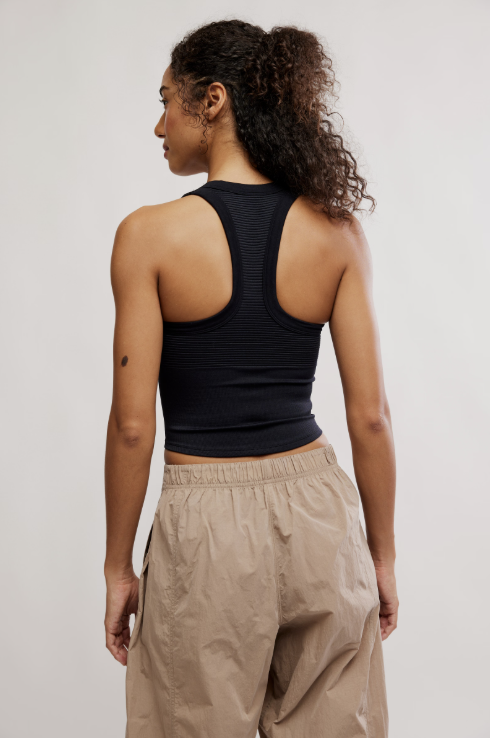 Person wearing a black tank top and beige pants against a plain background