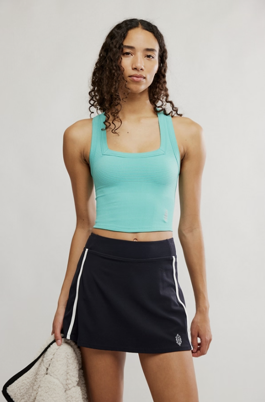 Woman wearing a turquoise tank top and black skirt with a white stripe on a plain background