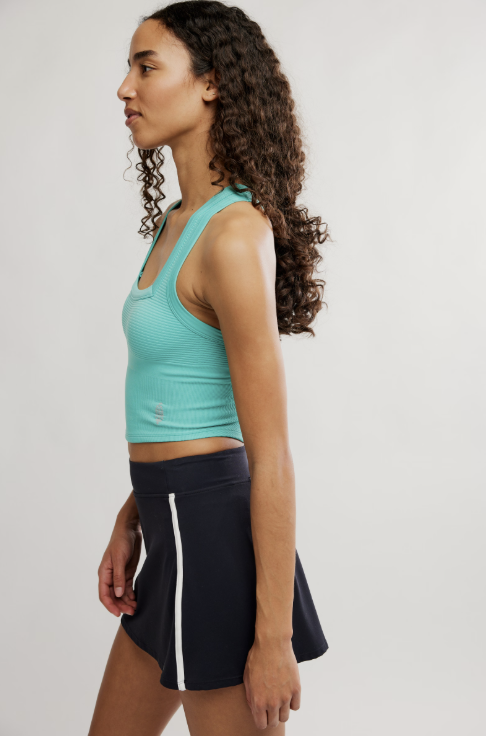 Woman wearing a teal tank top and black skirt with a white stripe on a plain background