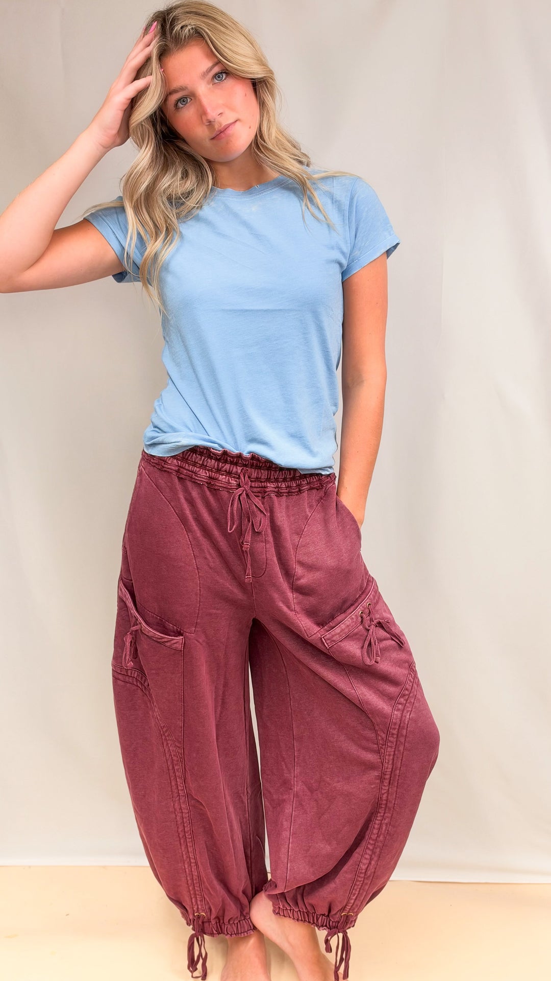 Woman wearing maroon parachute pants with drawstring details with blue shirt on plain background
