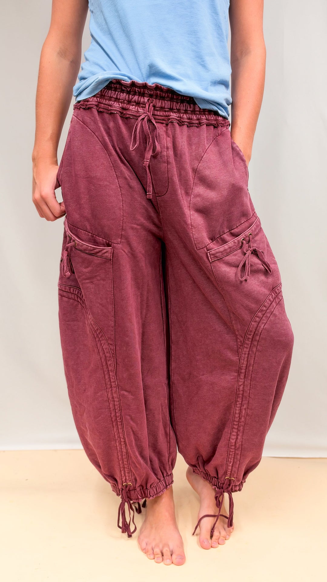 Woman wearing maroon parachute pants with drawstring detail and blue shirt on plain background