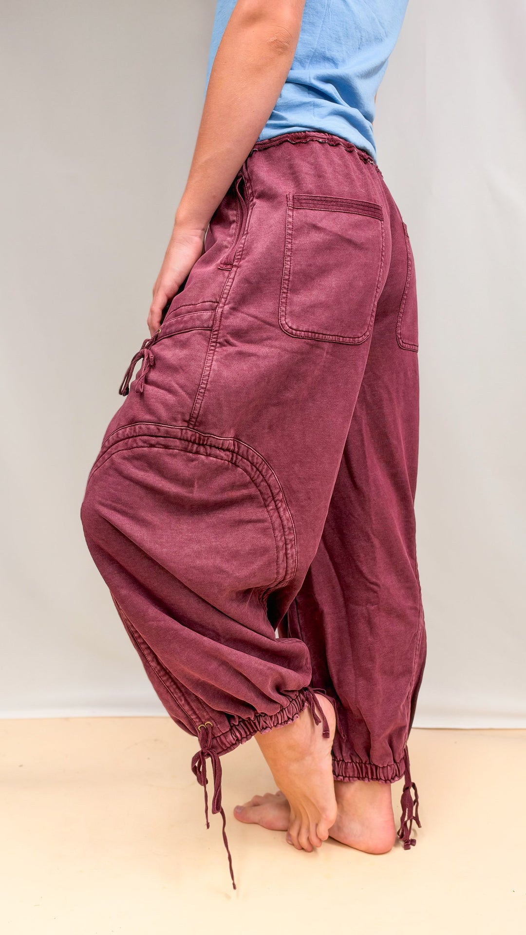 Woman wearing maroon parachute pants with drawstring detail and blue shirt on plain background