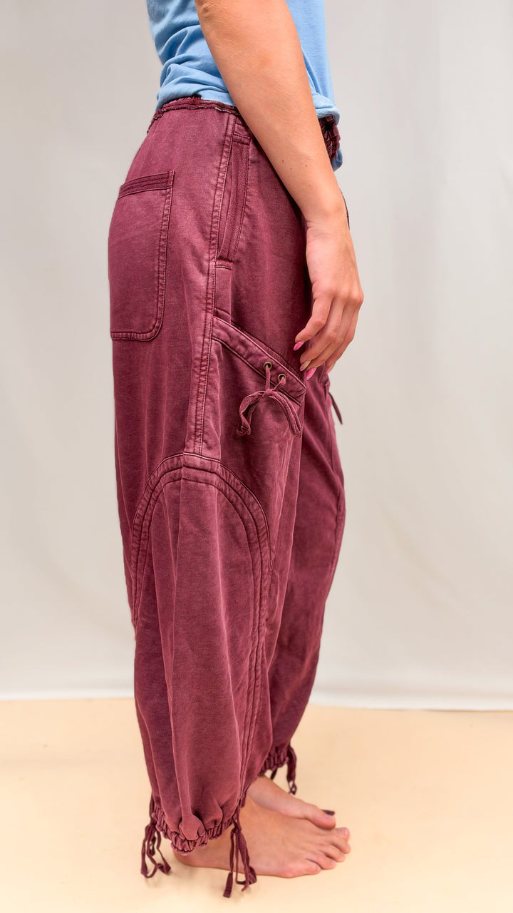 Woman wearing maroon parachute pants with drawstring detail and blue shirt on plain background