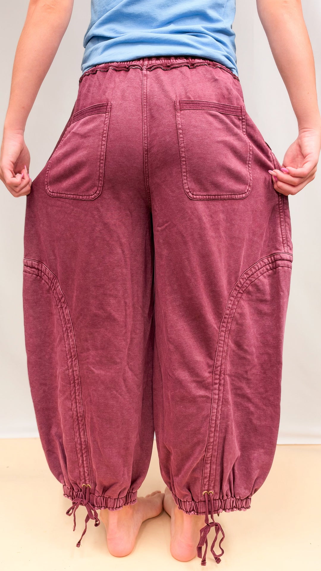 Woman shown from back wearing maroon parachute pants and blue shirt on plain background