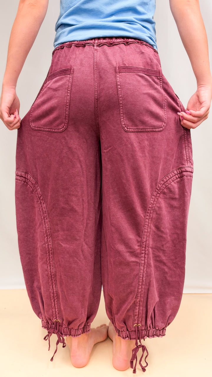 Woman shown from back wearing maroon parachute pants and blue shirt on plain background