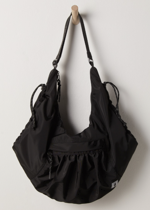 Black tote bag hanging on wooden post on plain white wall