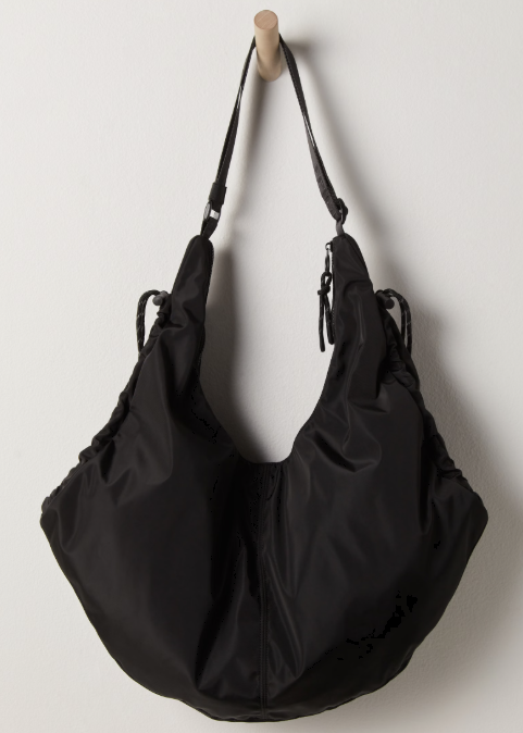 Black tote bag hanging on wooden peg on plain white wall.