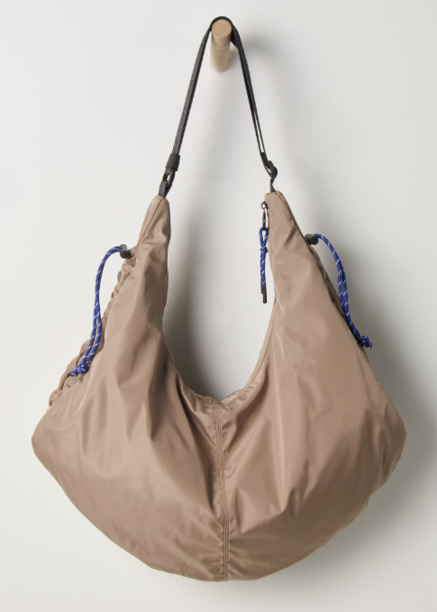 Beige tote bag hanging on wooden peg on plain background.