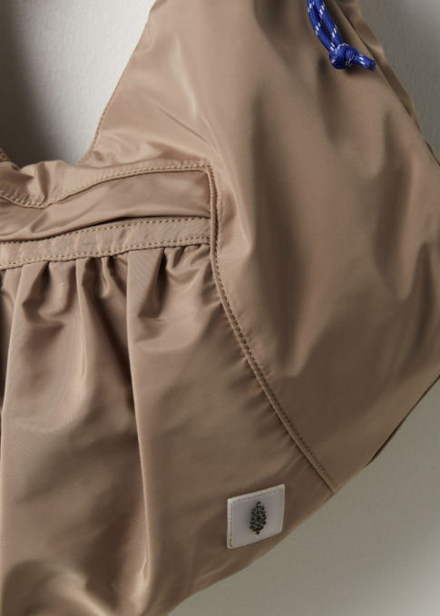 Close up of beige tote bag with logo patch and blue zipper pulls on plain background